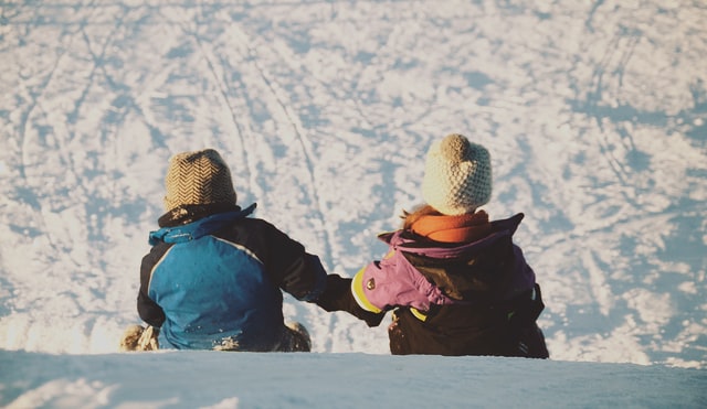 kids in winter jackets hold hands on top of snowy hill